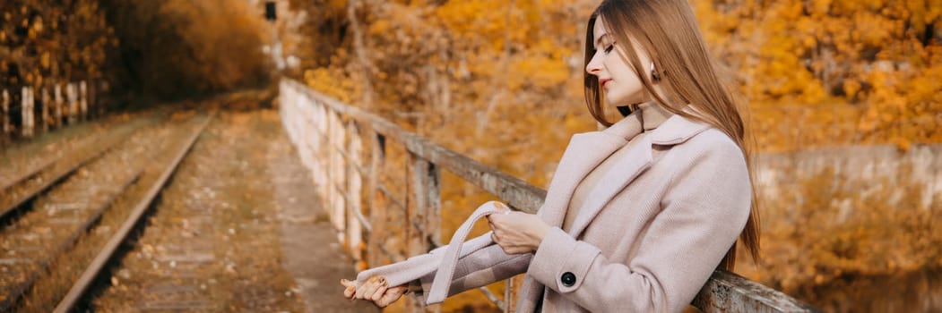 A beautiful long-haired woman walks through the autumn streets. Railway, autumn leaves, a woman in a light coat.