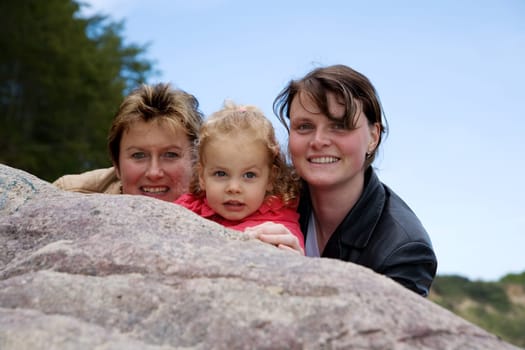 Mother,daughter and grandchild together in front of a blue,slightly cloudy sky
