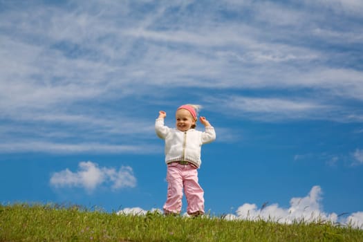 A little girl cheering on a green meadow against a blue sky