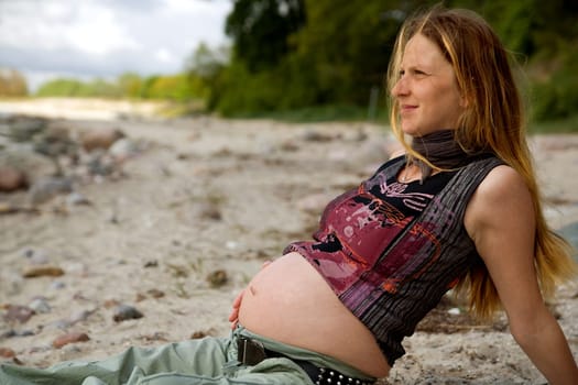 Young pregnant woman sitting relaxed on the beach