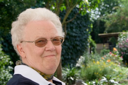 A senior citizen sits in the greenery and enjoys the warm sun and the beauty of her flowers.