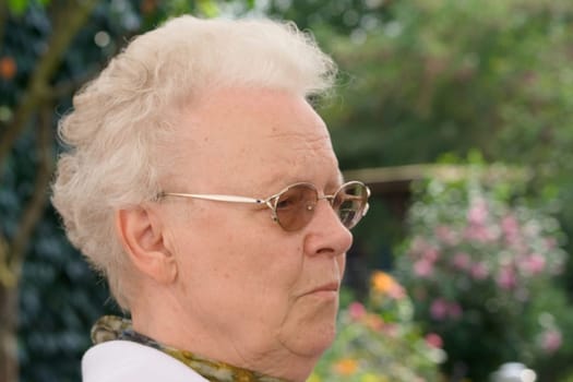 A senior citizen sits in the greenery and enjoys the warm sun and the beauty of her flowers.