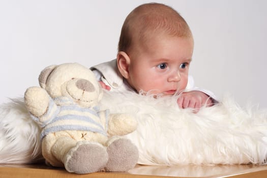Small child lies on a white fur and looks dreamily in one direction