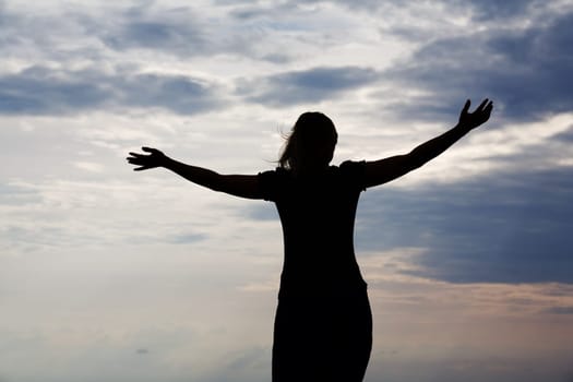 Silhouette of a woman in front of a cloudy sky,the woman stretching out her arms
