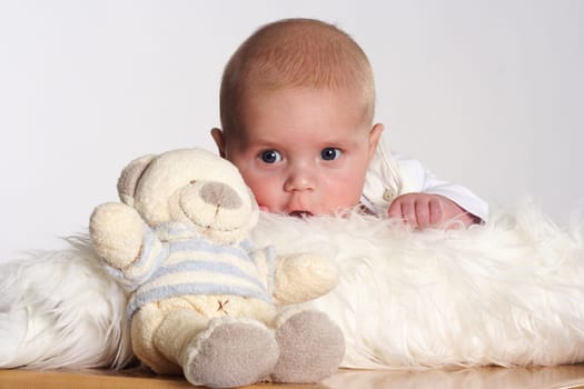 Small child lying on a white fur with a teddy bear