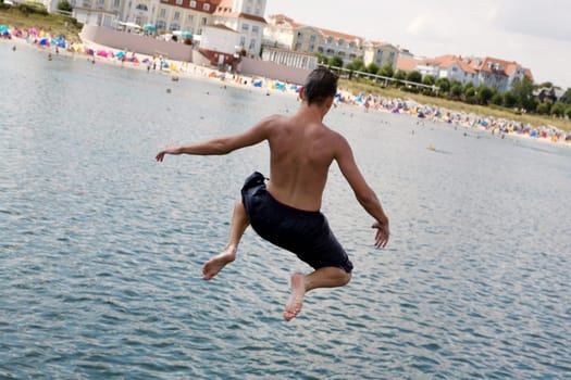 A young man jumps into the water,the beach can be seen in the background