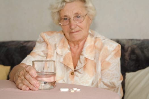 An elderly lady with a glass of water and tablets,focus on the tablets