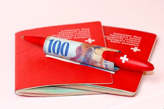 Two Swiss passports with 100 CHF and a ballpoint pen