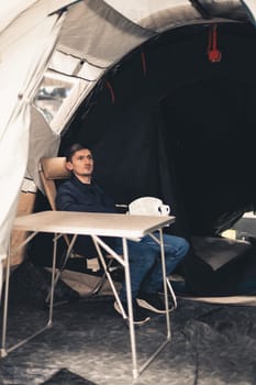 One young Caucasian man in a blue jacket sits and dreams at a table in a tent in a store, close-up side view.