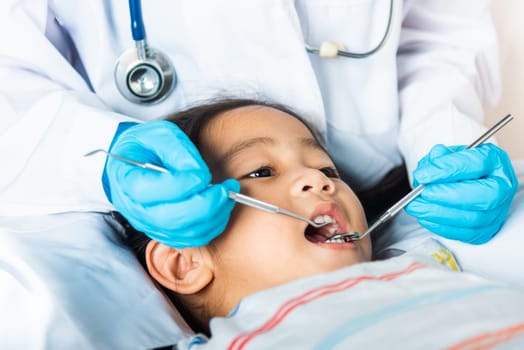 Dental kid health examination. Doctor examines oral cavity of little child uses mouth mirror to checking teeth cavity, Asian dentist making examination procedure for smiling cute little girl