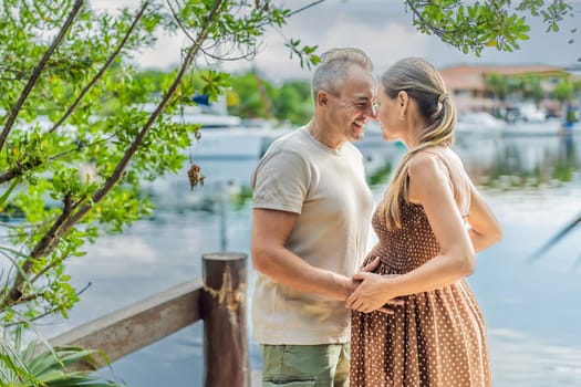 A happy, mature couple over 40, enjoying a leisurely walk on the waterfront, their joy evident as they embrace the journey of pregnancy later in life.