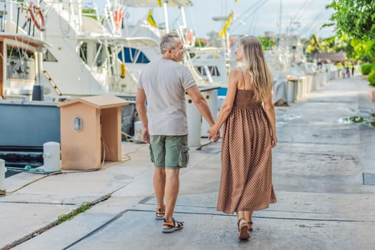 A happy, mature couple over 40, enjoying a leisurely walk on the waterfront, their joy evident as they embrace the journey of pregnancy later in life.
