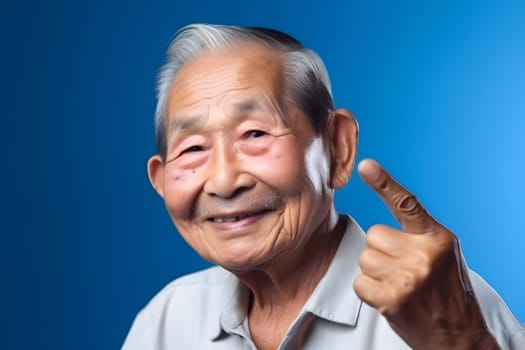 Asian grandfather looking and smiling with rised index finger on blue background. Neural network generated in May 2023. Not based on any actual person, scene or pattern.
