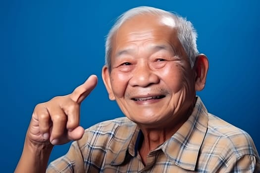 Asian grandfather looking and smiling with rised index finger on blue background. Neural network generated in May 2023. Not based on any actual person, scene or pattern.