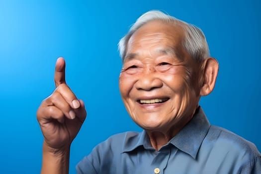 Asian grandfather looking and smiling with rised index finger on blue background. Neural network generated in May 2023. Not based on any actual person, scene or pattern.