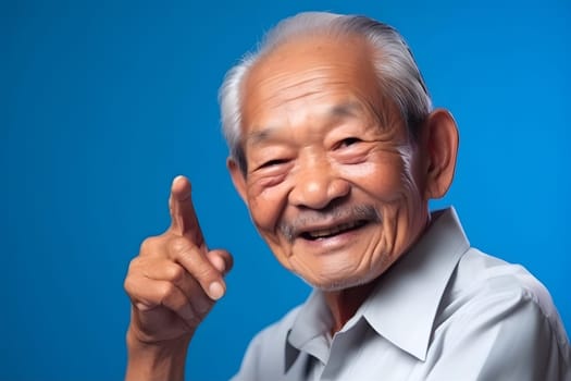 Asian grandfather looking and smiling with rised index finger on blue background. Neural network generated in May 2023. Not based on any actual person, scene or pattern.