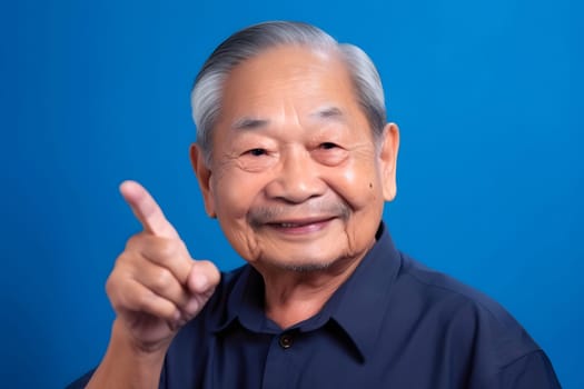 Asian grandfather looking and smiling with rised index finger on blue background. Neural network generated in May 2023. Not based on any actual person, scene or pattern.