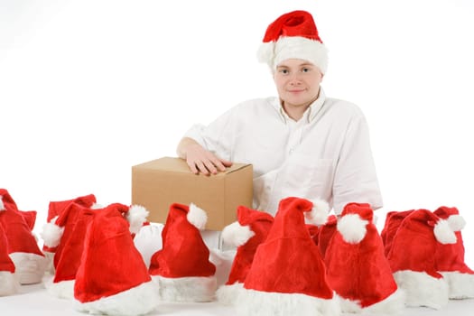 A young man in a Santa Claus hat sits among many Christmas hats and holds a package