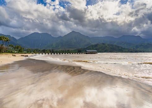 Hanalei Pier and beach are framed by dramatic mountains and sky in this scenic view of the north shore of Kauai.