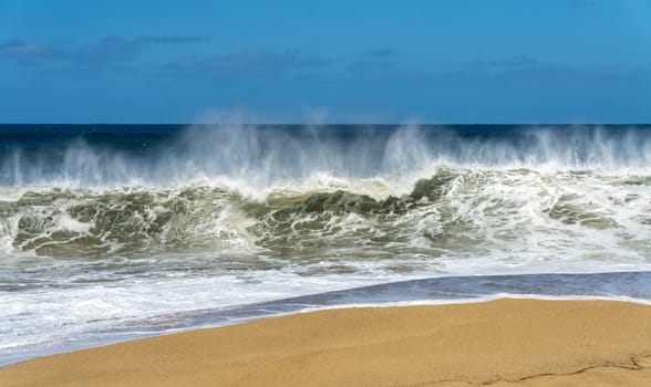 Ocean waves crashing on the sandy beach with the turquoise water rippling and splashing at Lumahai Beach.