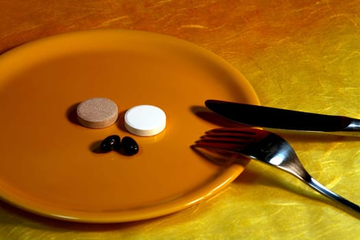 Vitamin tablets on a yellow plate with a knife and fork