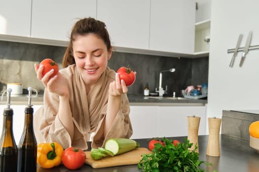 Portrait of beautiful woman cooking in the kitchen, chopping vegetables on board, holding tomatoes, lead healthy lifestyle with preparing fresh salads, vegan meals.