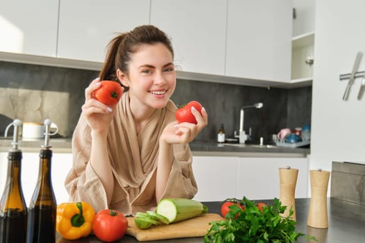 Portrait of beautiful woman cooking in the kitchen, chopping vegetables on board, holding tomatoes, lead healthy lifestyle with preparing fresh salads, vegan meals.