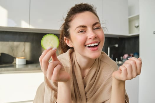 Portrait of happy, smiling young woman in the kitchen, cooking, chopping zucchini, holding vegetables and looking happy, preparing vegan food meal at home.