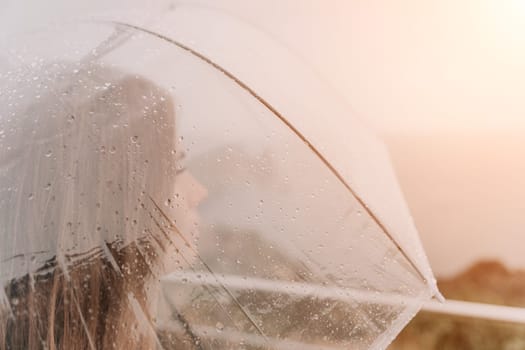 Woman rain park. Happy woman portrait wearing a raincoat with transparent umbrella outdoors on rainy day in park near sea. Girl on the nature on rainy overcast day