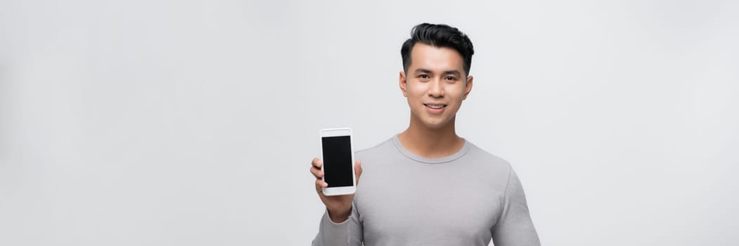 Smiling young man holds a modern smartphone in his hand on a blank screen