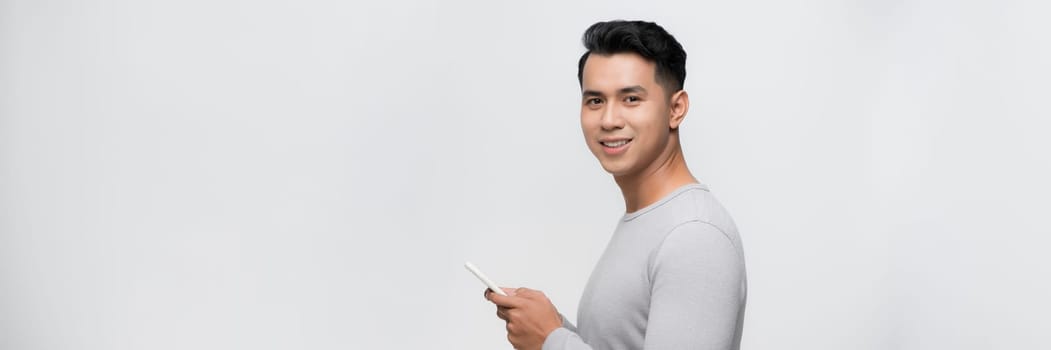  Handsome young man using his phone with smile while standing against white background.