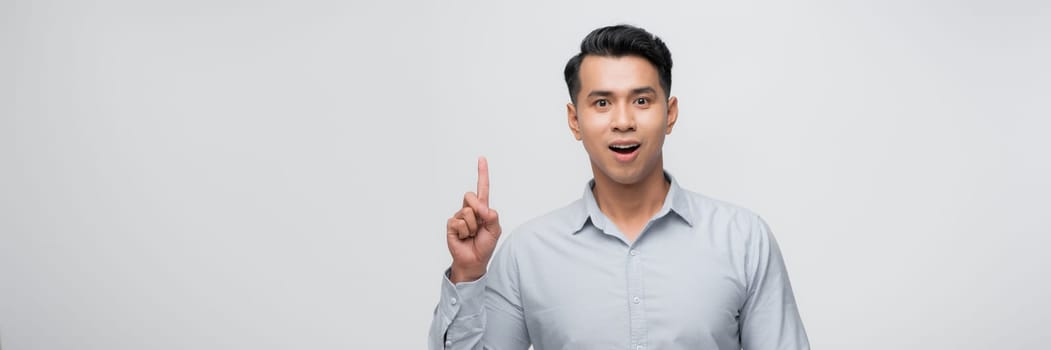 Attractive young man pointing up with his finger isolated on gray background