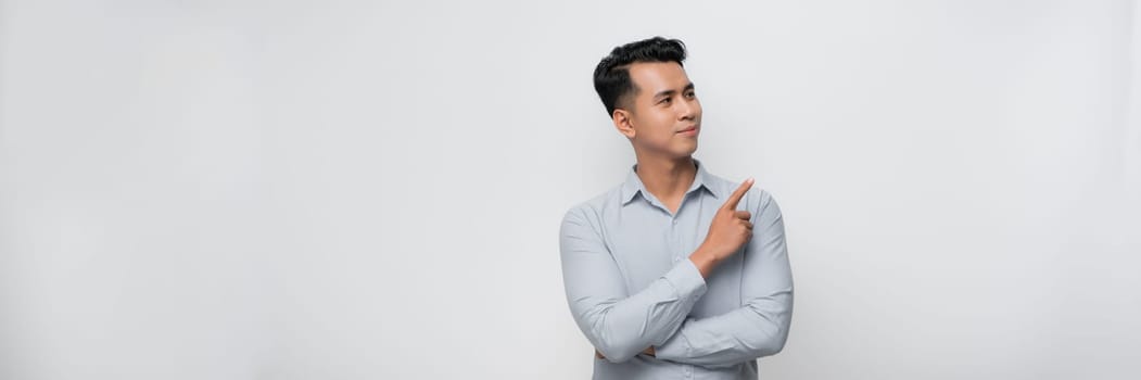 Young handsome man with a big smile on face, pointing with hand and finger to the side looking at the camera.