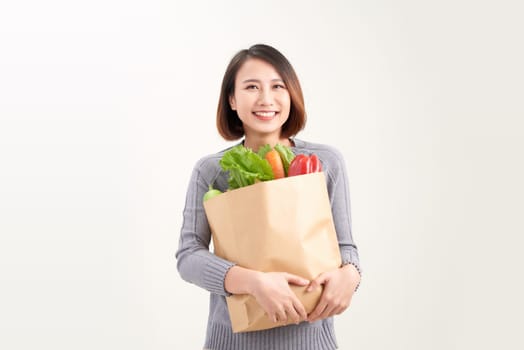 Young asian woman smiles embraces paper bag with fresh products returns from supermarket 