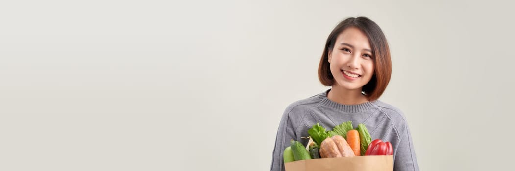 Smiling asian woman happily holding a bag of vegetables, healthy eating and wellness concept.