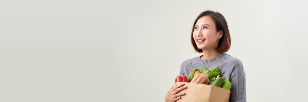 Happy woman holding paper bag full of fresh vegetable groceries isolated on white copy space background.