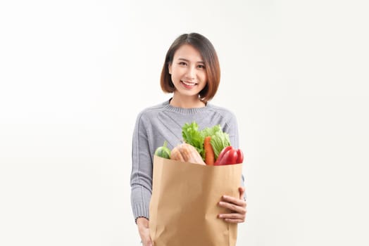Smiling woman holding a shopping bag full of groceries posing on a studio white background.
