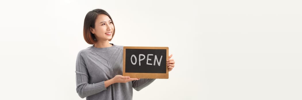 Young beautiful asian woman wearing apron holding open blackboard over isolated white background