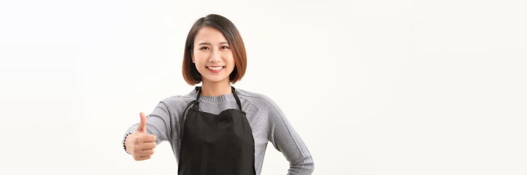 Cheerful young pretty female cafe staff in black apron show support or like gesture.