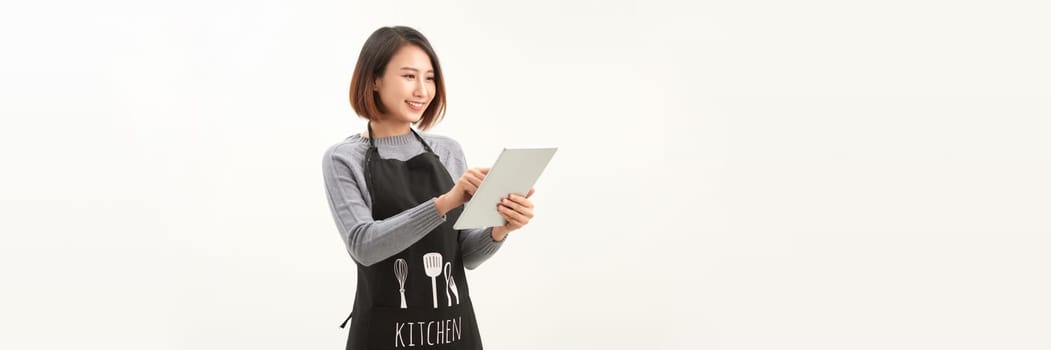 Friendly cute female barista in black apron smiling at camera, using digital tablet to manage cafe orders