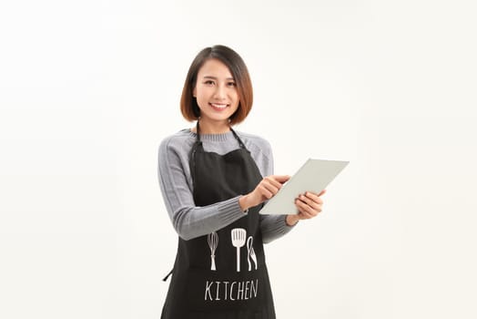 Friendly cute female barista in black apron smiling at camera, using digital tablet to manage cafe orders