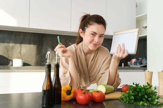 Portrait of woman cooking in the kitchen, reading her notes, checking recipe while preparing meal, making breakfast salad, writing down grocery list.