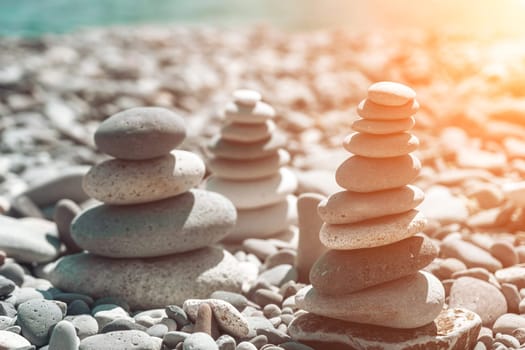 Pyramid stones on the seashore with warm sunset on the sea background. Happy holidays. Pebble beach, calm sea, travel destination. Concept of happy vacation on the sea, meditation, spa, calmness.