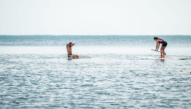 Sea woman and man on sup. Silhouette of happy young woman and man, surfing on SUP board, confident paddling through water surface. Idyllic sunset. Active lifestyle at sea or river