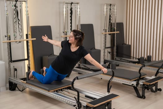 Overweight caucasian woman doing pilates exercises on a reformer