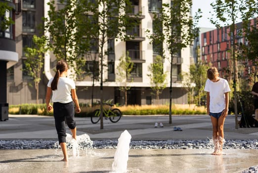 Happy teenage girl dancing in a fountain in a city park on a hot summer day. High quality photo