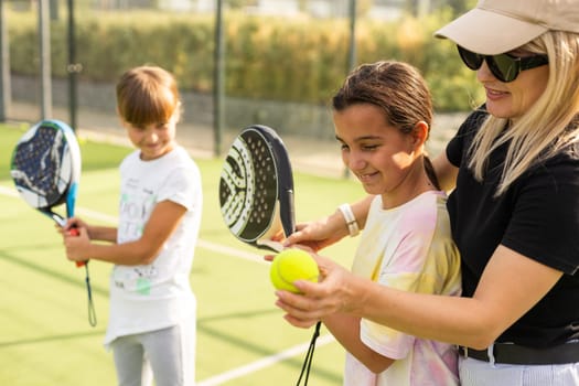 Cheerful coach teaching child to play tennis while both standing on tennis court. High quality photo