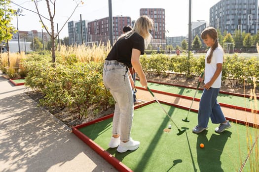 Mother and her little daughter practicing to hit the ball at the course. High quality photo