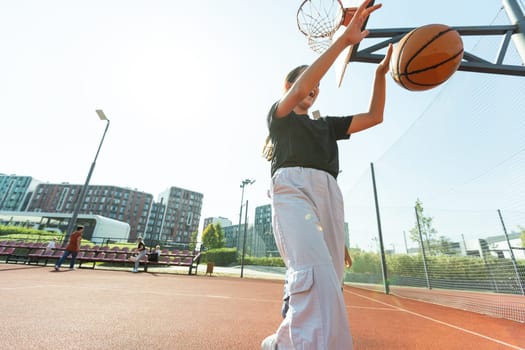 Concept of sports, hobbies and healthy lifestyle. Young athletic girl is training to play basketball on modern outdoor basketball court. Happy woman. High quality photo