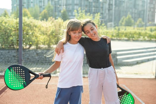 Kids and sports concept. Portrait of smiling girls posing outdoor on padel court with rackets and tennis balls. High quality photo
